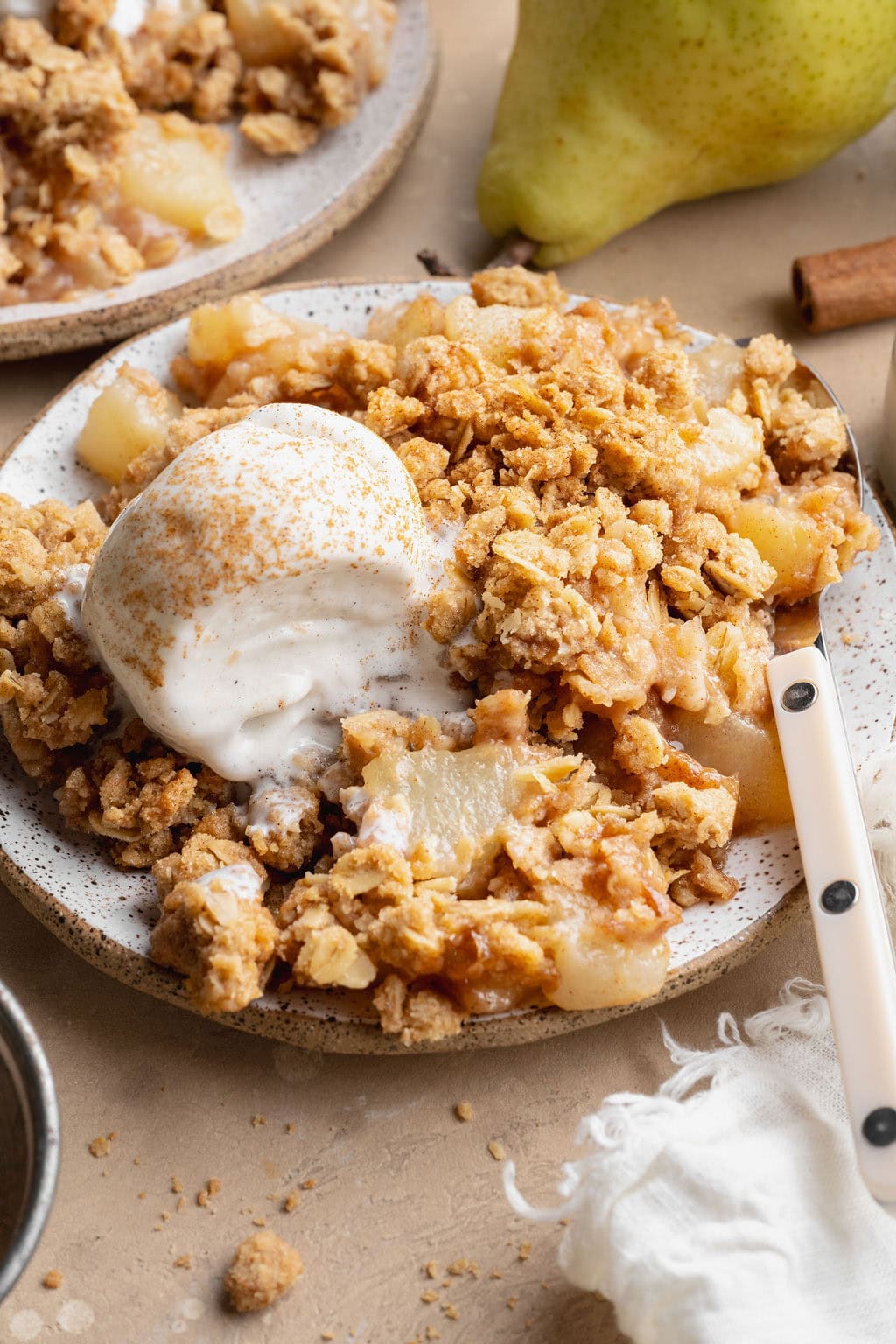 A serving of pear crisp on a plate topped with ice cream, a spoon on the side.