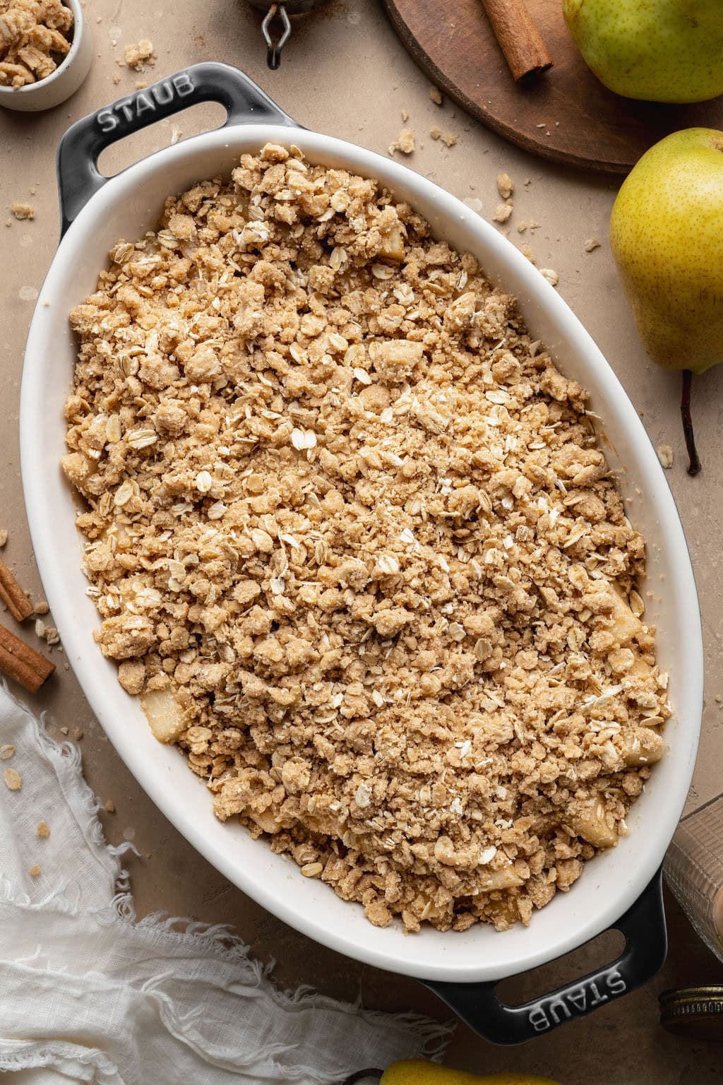 An unbaked pear crisp in an oval baking dish.