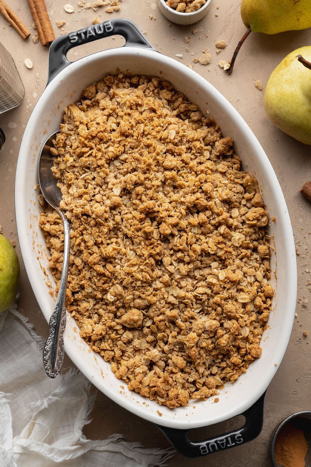A baked pear crisp in an oval baking dish with a spoon on the side.