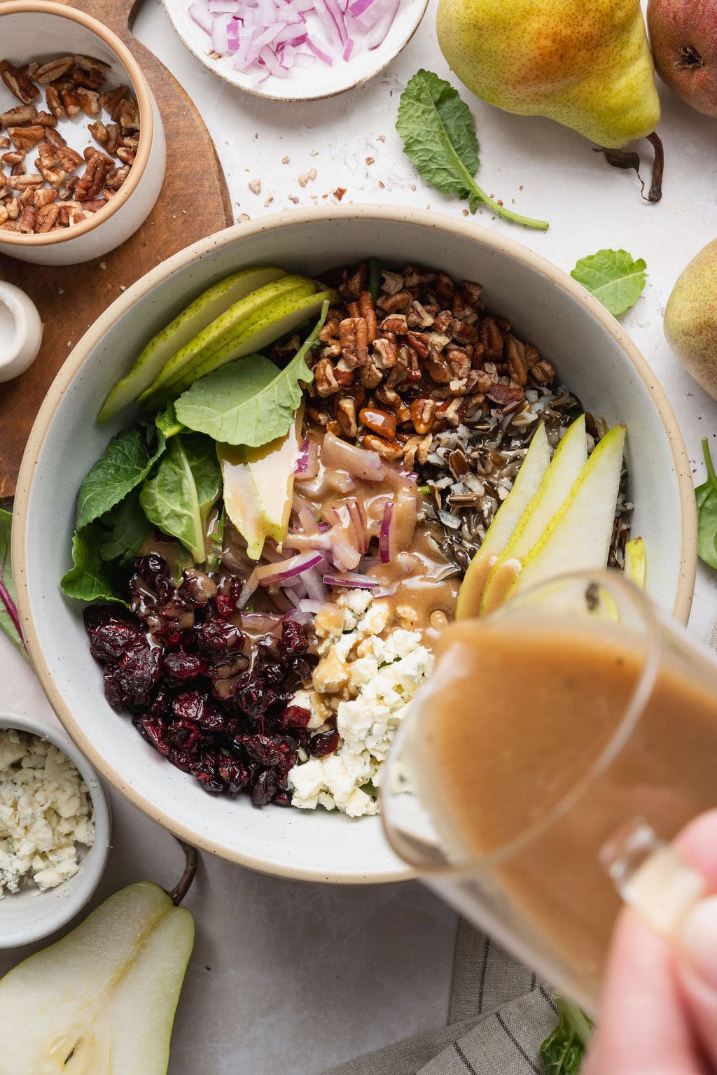 Balsamic vinaigrette being poured over pear salad ingredients in a bowl.