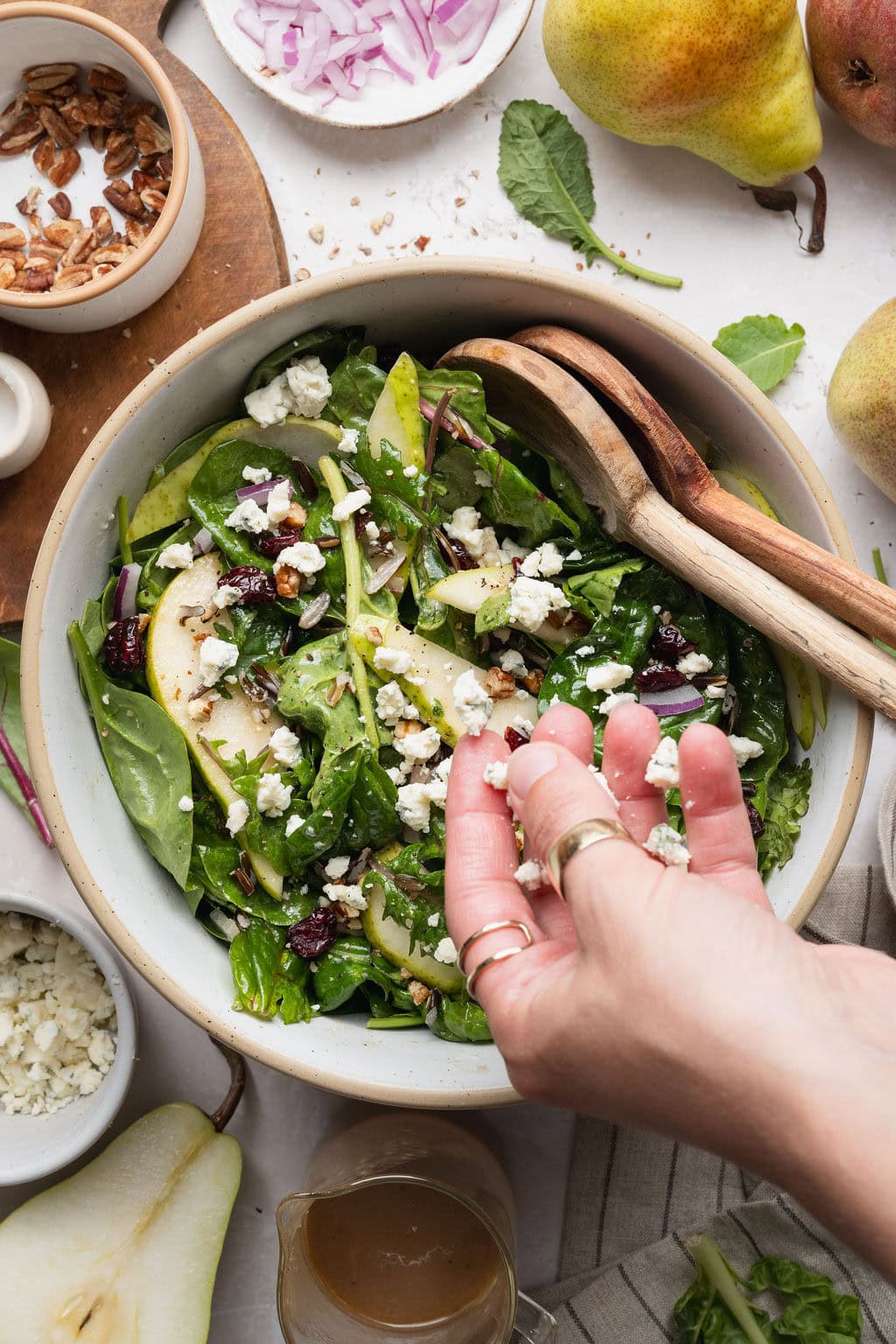 A woman's hand sprinkling blue cheese crumbles over a pear salad.