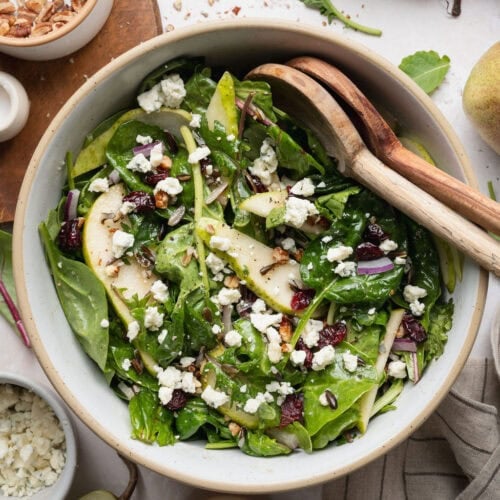 A bowl of pear salad with wooden serving spoons on the side.