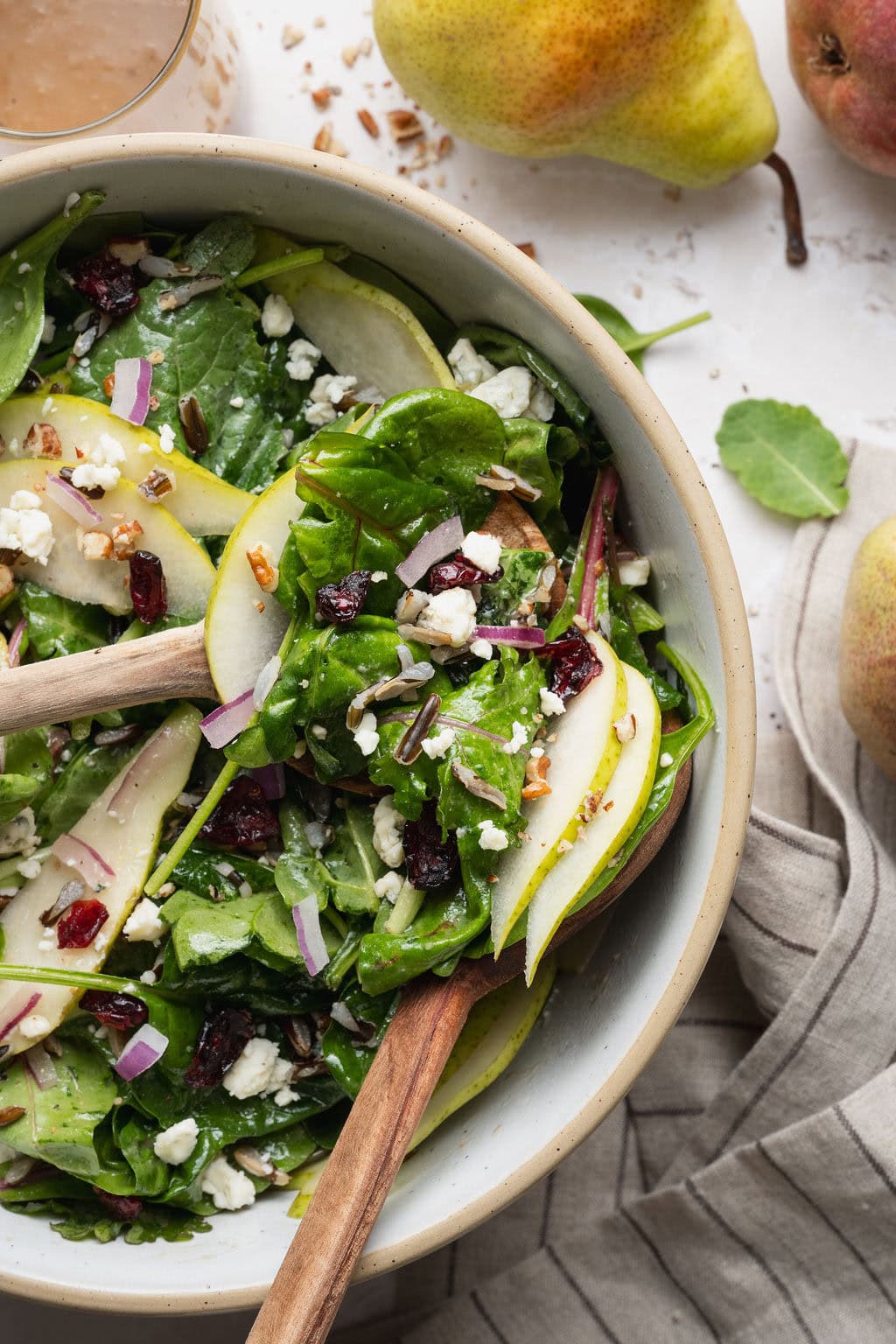 Wooden serving spoons lifting a scoop of pear salad from a bowl.