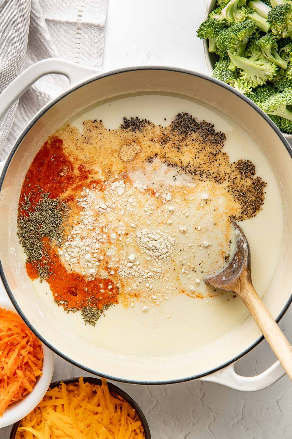 Seasonings being added to a pot of milk and broth for broccoli cheddar soup.