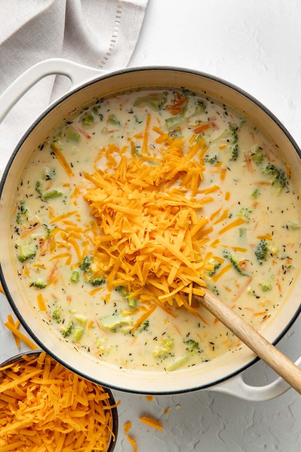 Shredded cheese being stirred into a pot of broccoli cheddar soup.