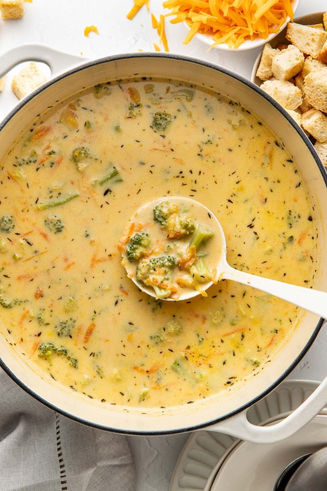 A ladle lifting a scoop of broccoli cheddar soup from a pot.