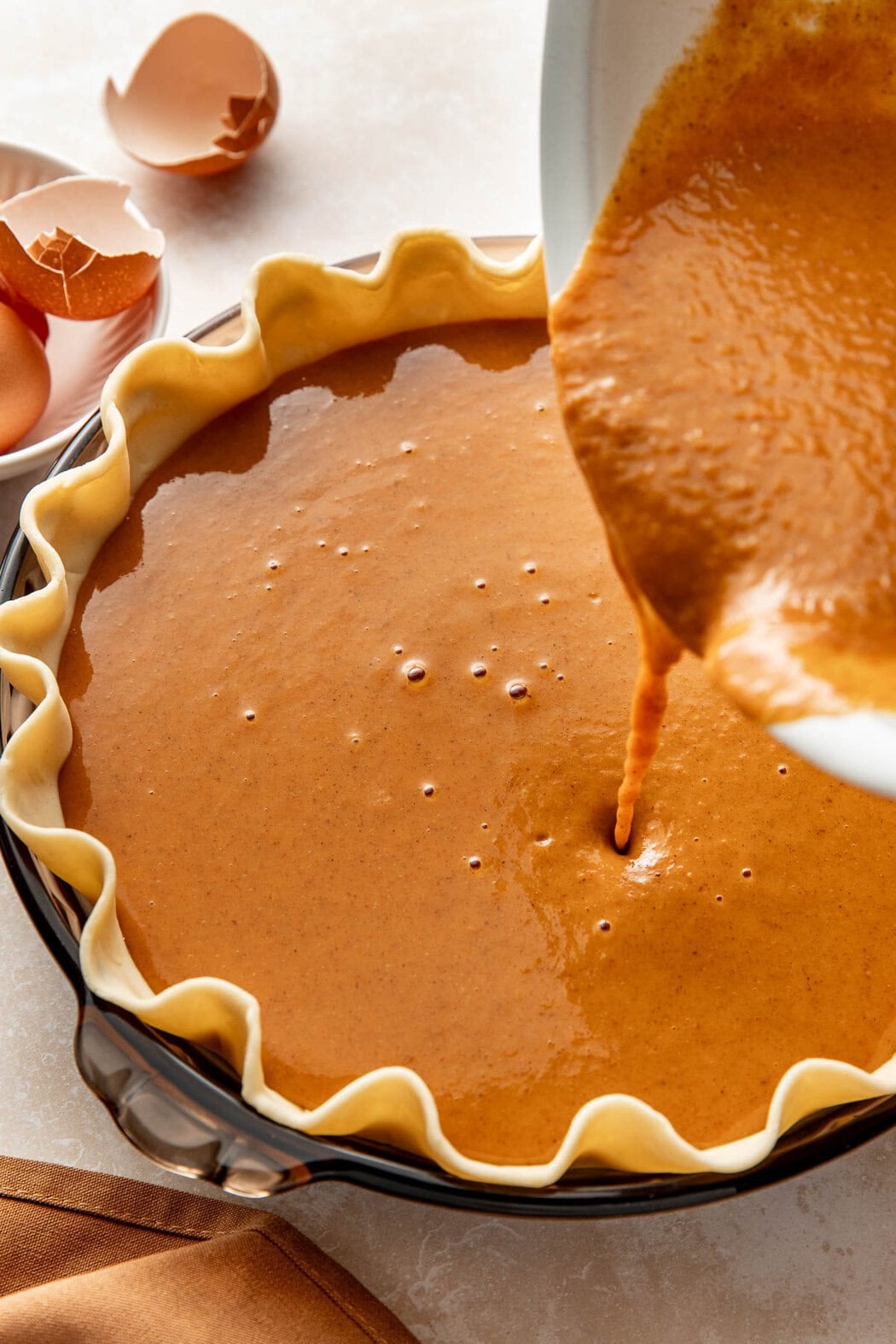 Pumpkin pie filling being poured into a prepared crust.