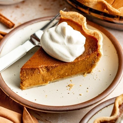 A slice of pumpkin pie on a plate topped with whipped cream.