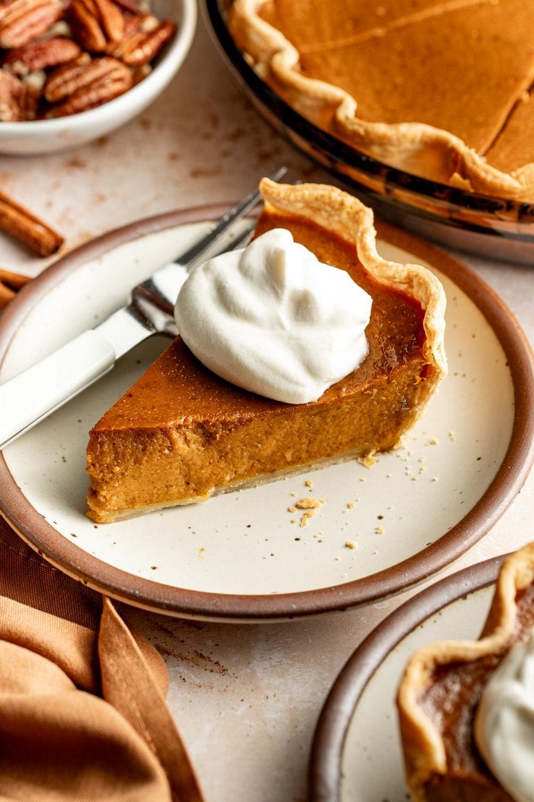 A slice of pumpkin pie on a plate topped with a dollop of whipped cream.