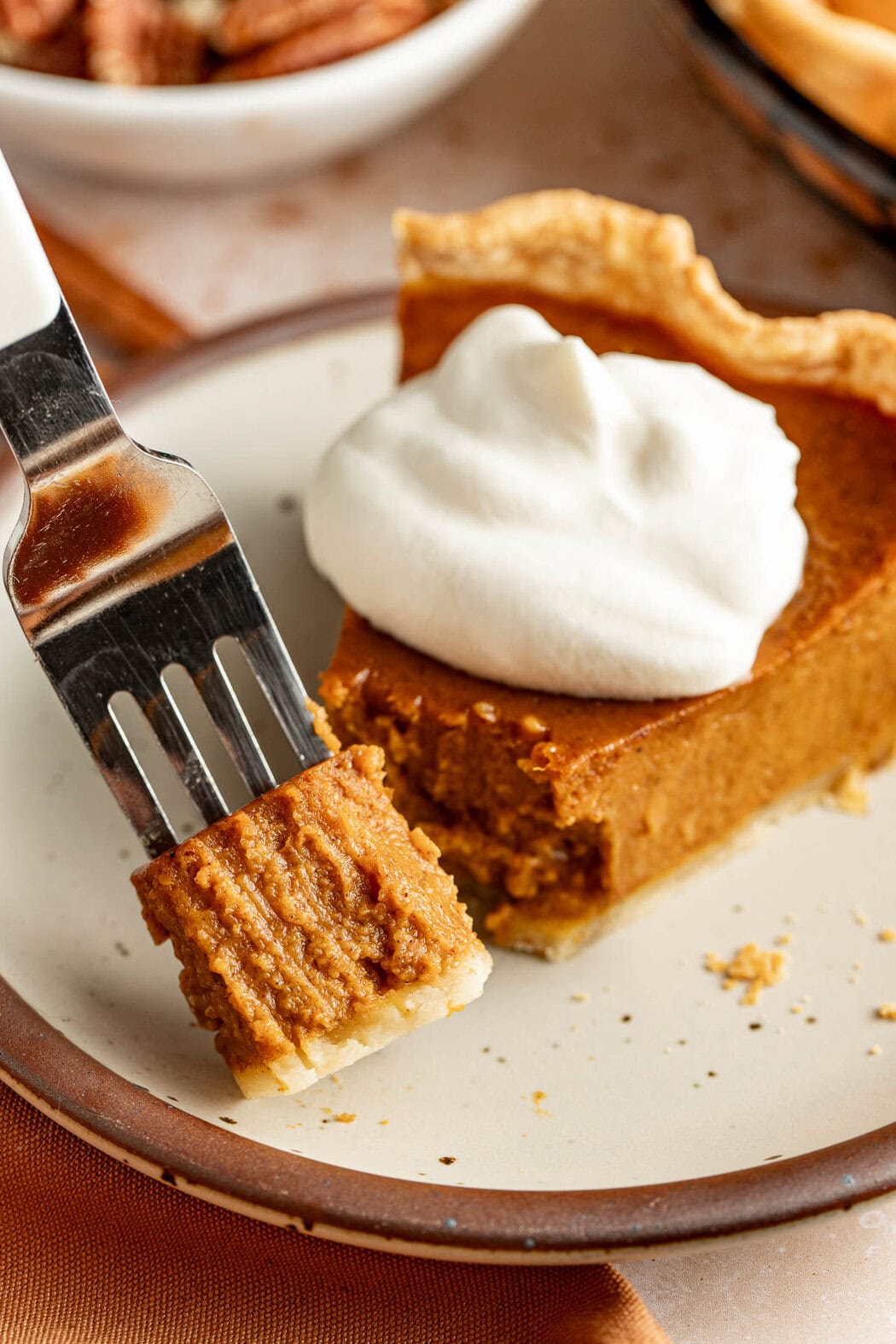 A slice of pumpkin pie on a plate topped with whipped cream, a fork holding a bite.