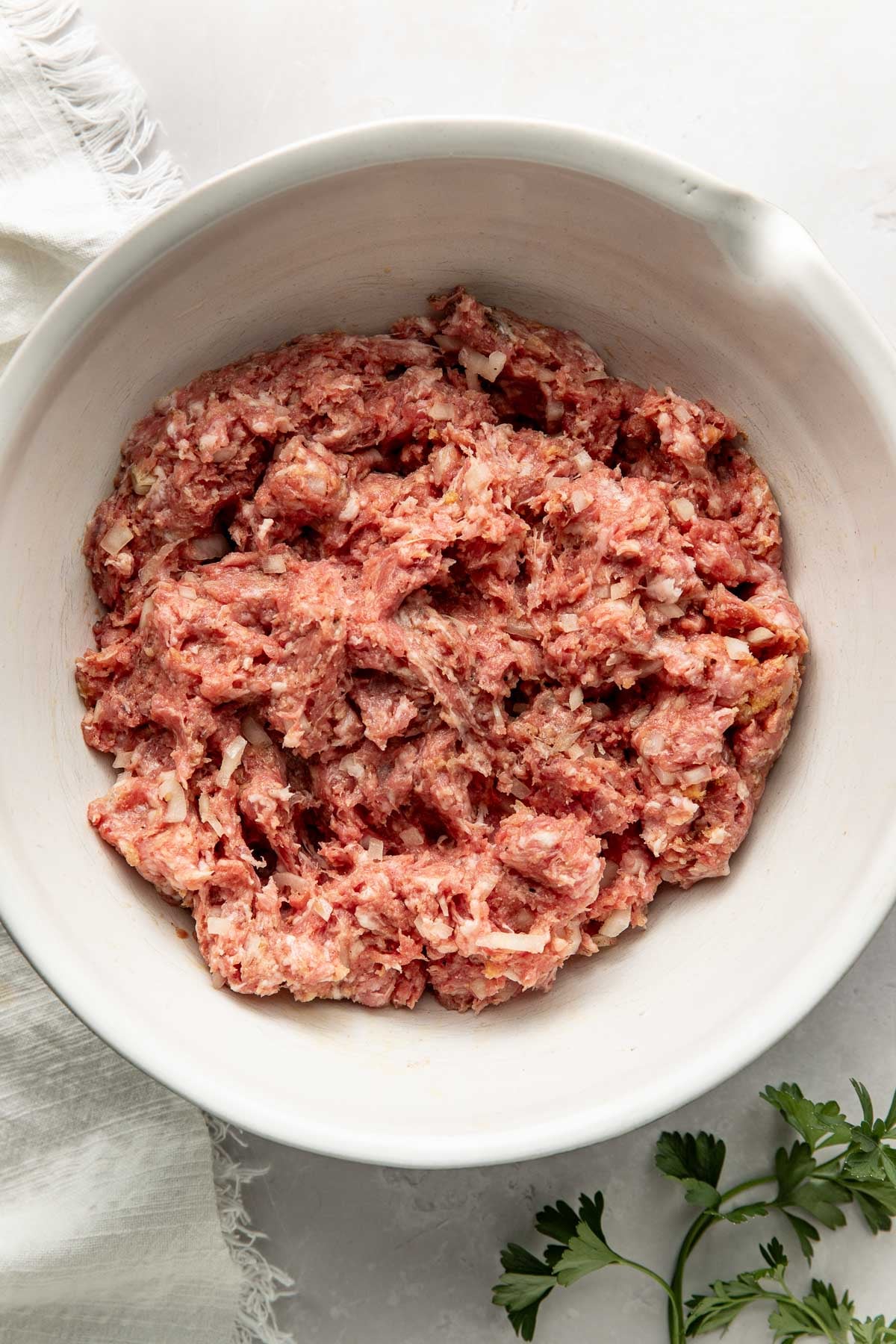 A raw meatball mixture in a white bowl.