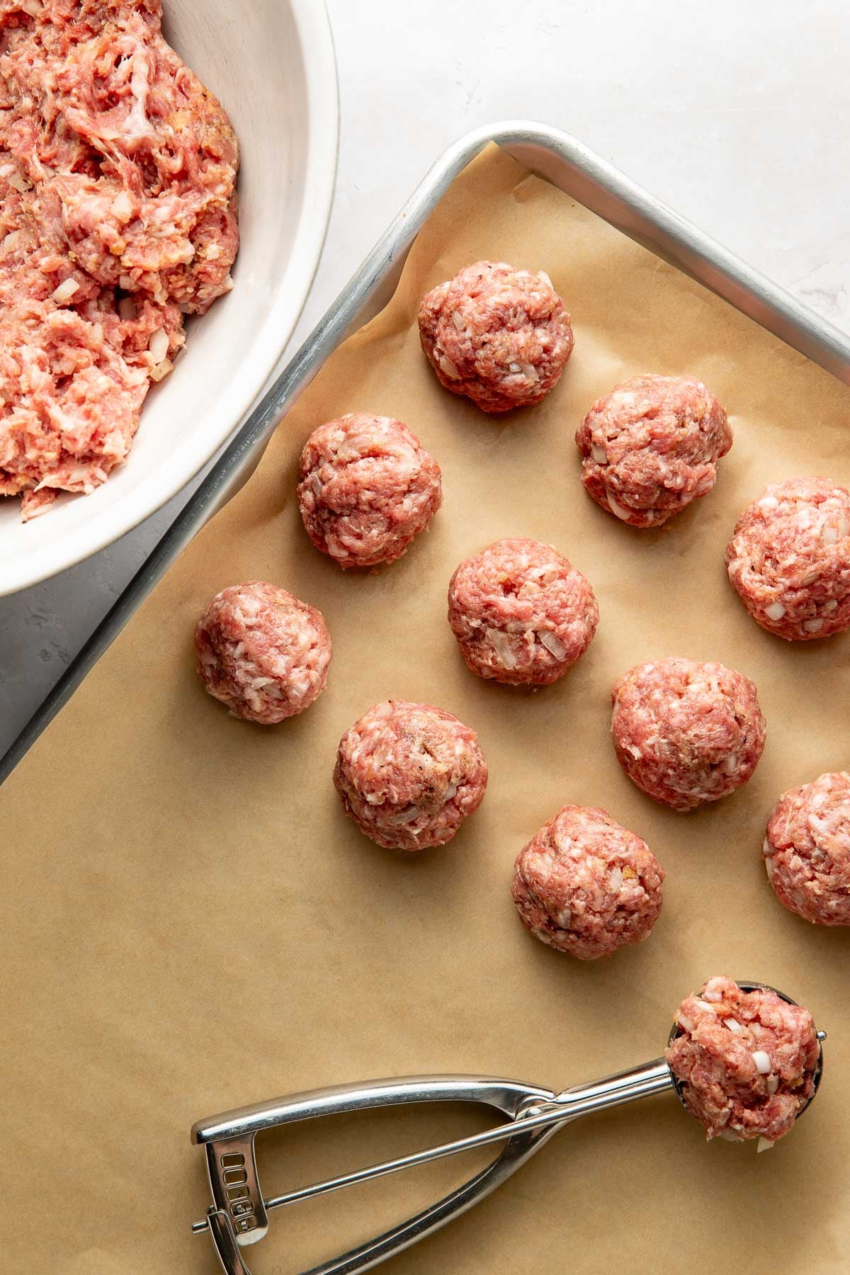 A Swedish meatball mixture being portioned with a cookie scoop and placed on a parchment-lined baking sheet.