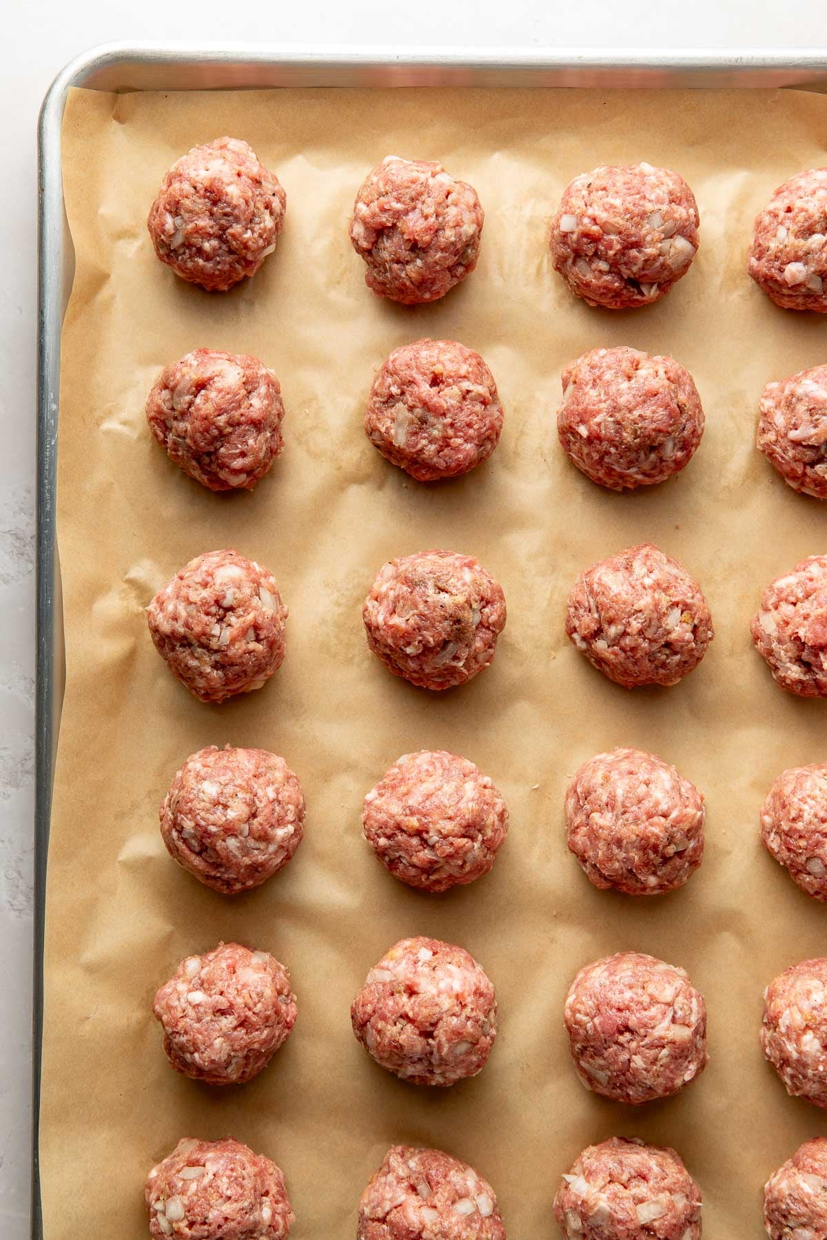 Raw Swedish meatballs on a parchment-lined baking sheet.