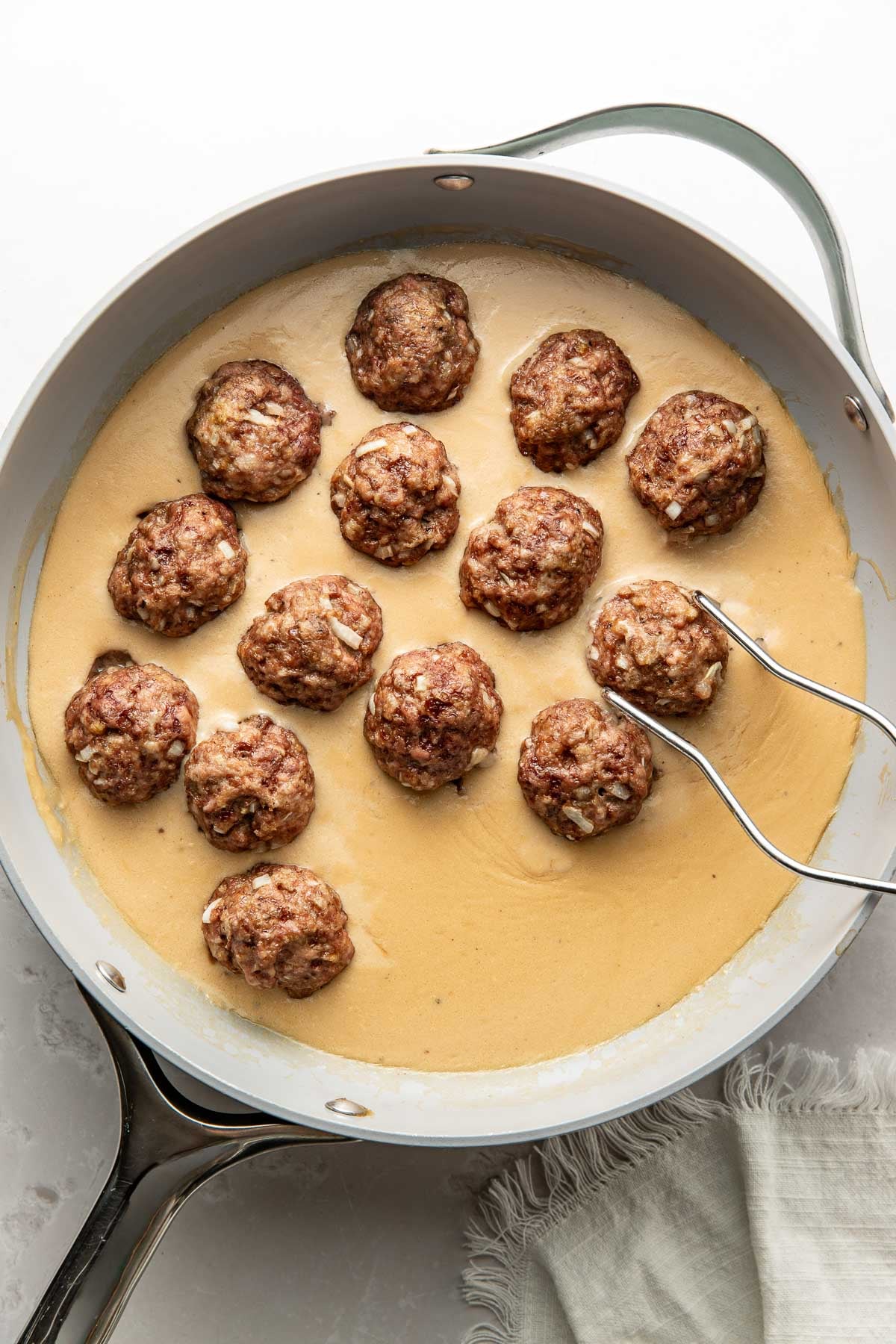 Swedish meatballs being placed in a skillet of sauce.
