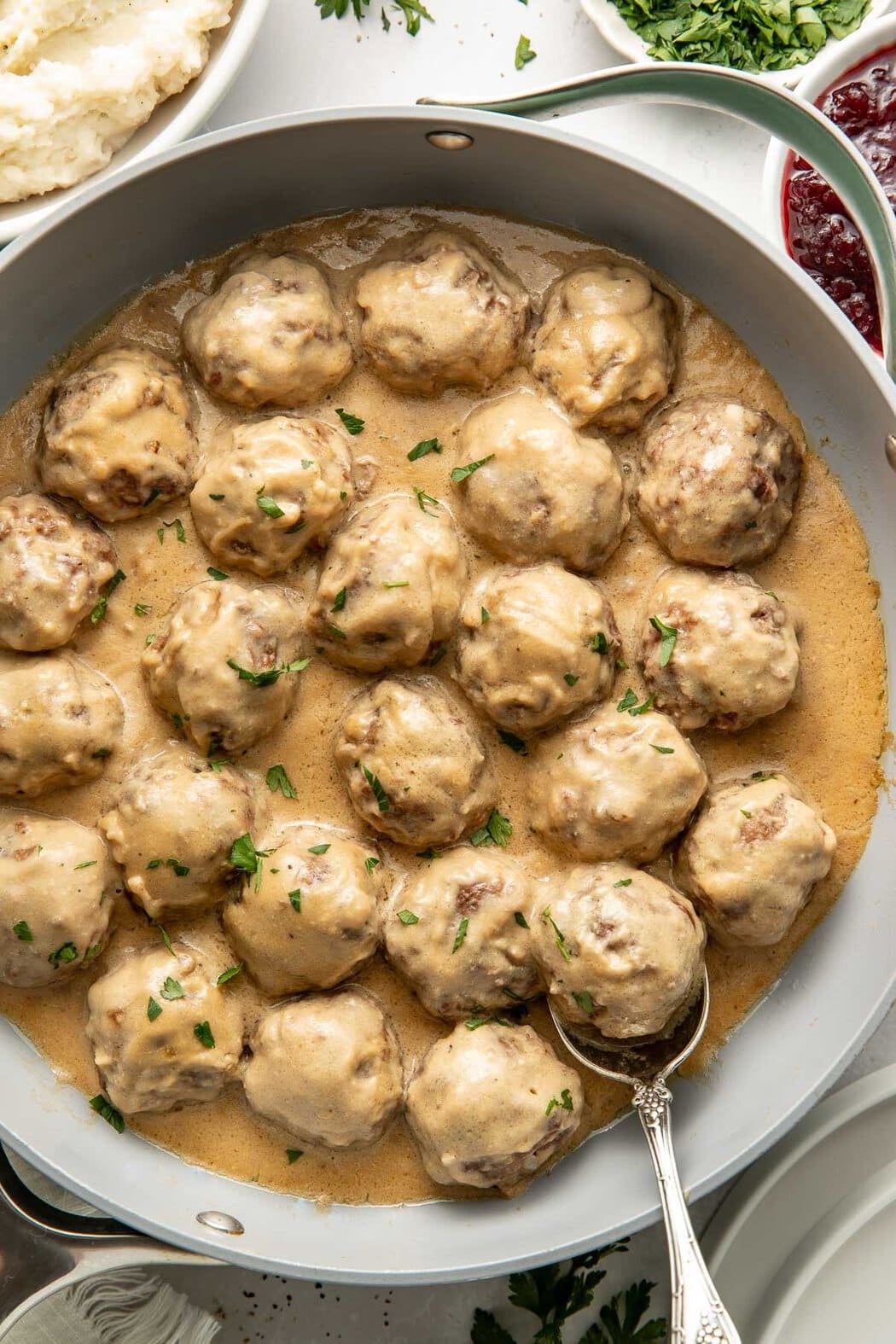 A skillet of Swedish meatballs with sauce, a spoon lifting one meatball.