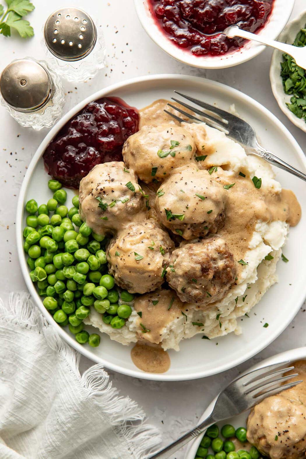 A plate of Swedish meatballs served over mashed potatoes with a side of peas and cranberry sauce. 