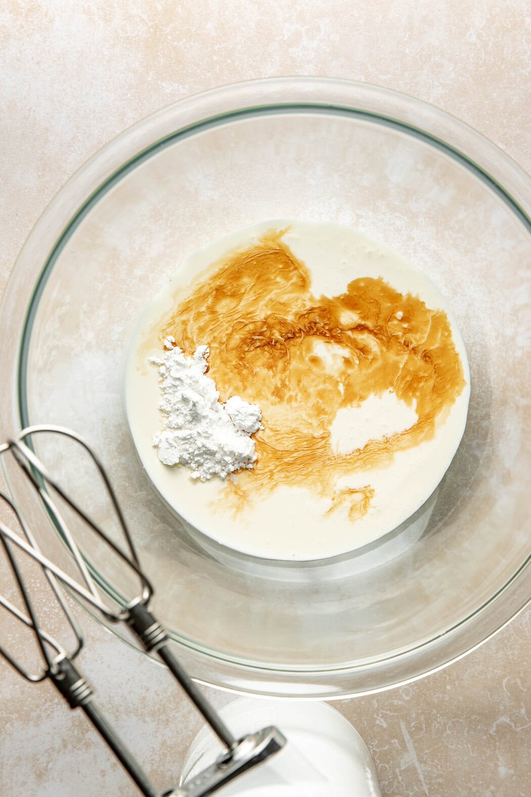 Whipped cream ingredients in a glass bowl next to a hand mixer.