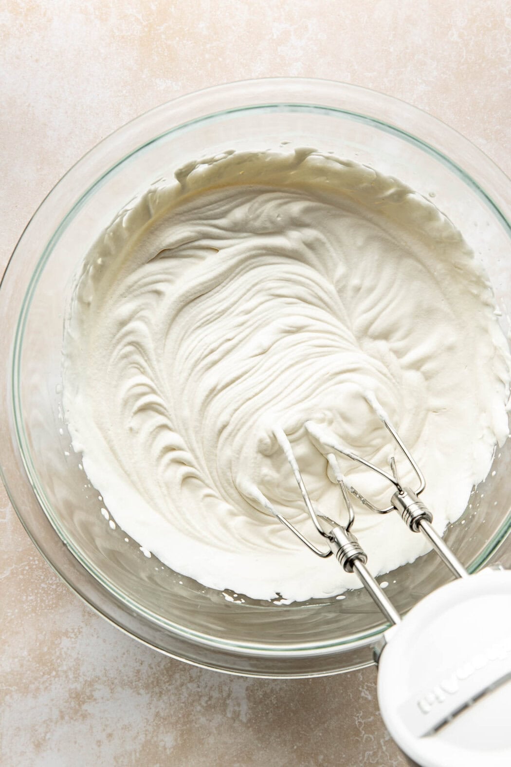 A hand mixer in a glass bowl, whipping ingredients to make whipped cream.