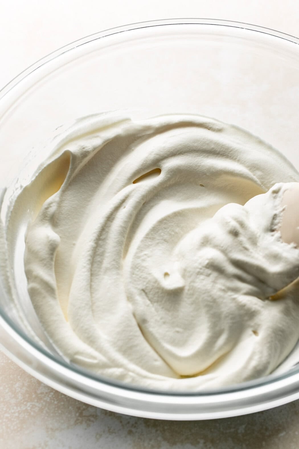 A rubber spatula sticking out of a bowl of homemade whipped cream.