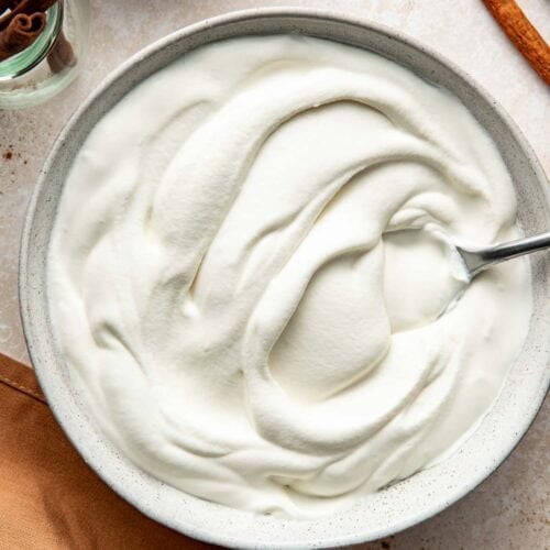 A bowl of homemade whipped cream with a spoon sticking out.