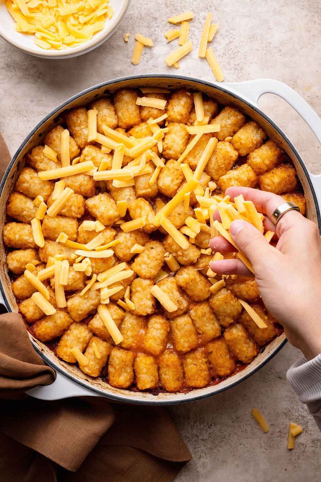 Shredded cheese being sprinkled over a pot of cheeseburger casserole topped with tater tots.