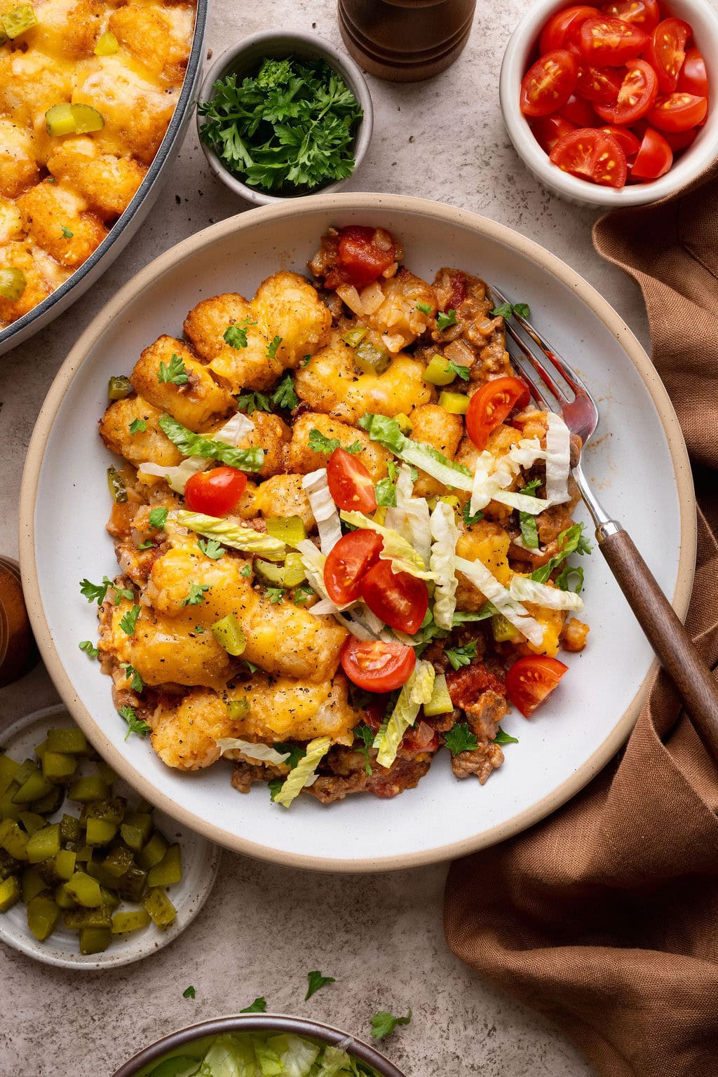 A serving of cheeseburger casserole in a bowl topped with shredded lettuce and tomatoes, a fork on the side.