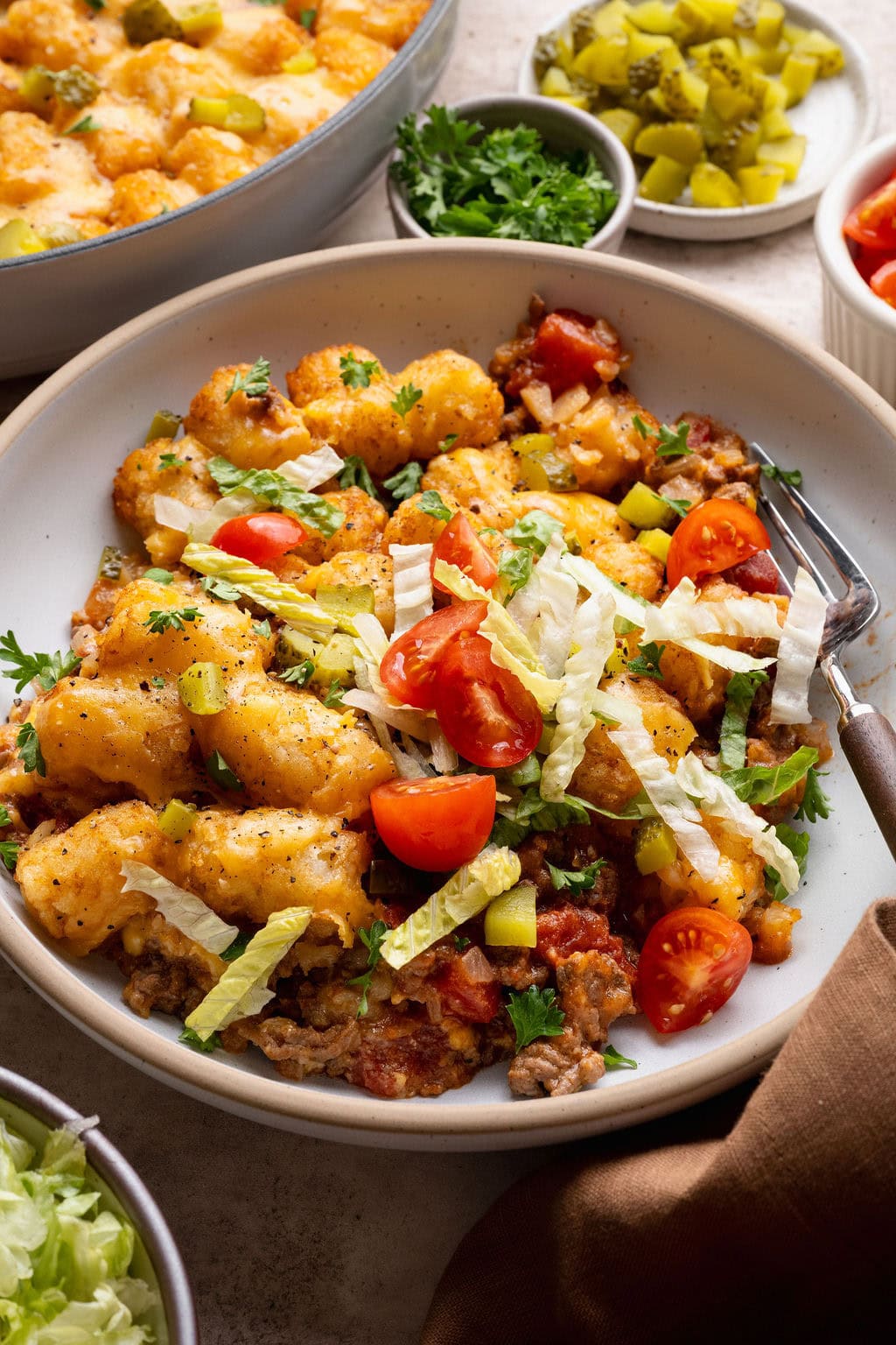 A serving of cheeseburger casserole in a bowl topped with shredded lettuce and tomatoes, a fork on the side.