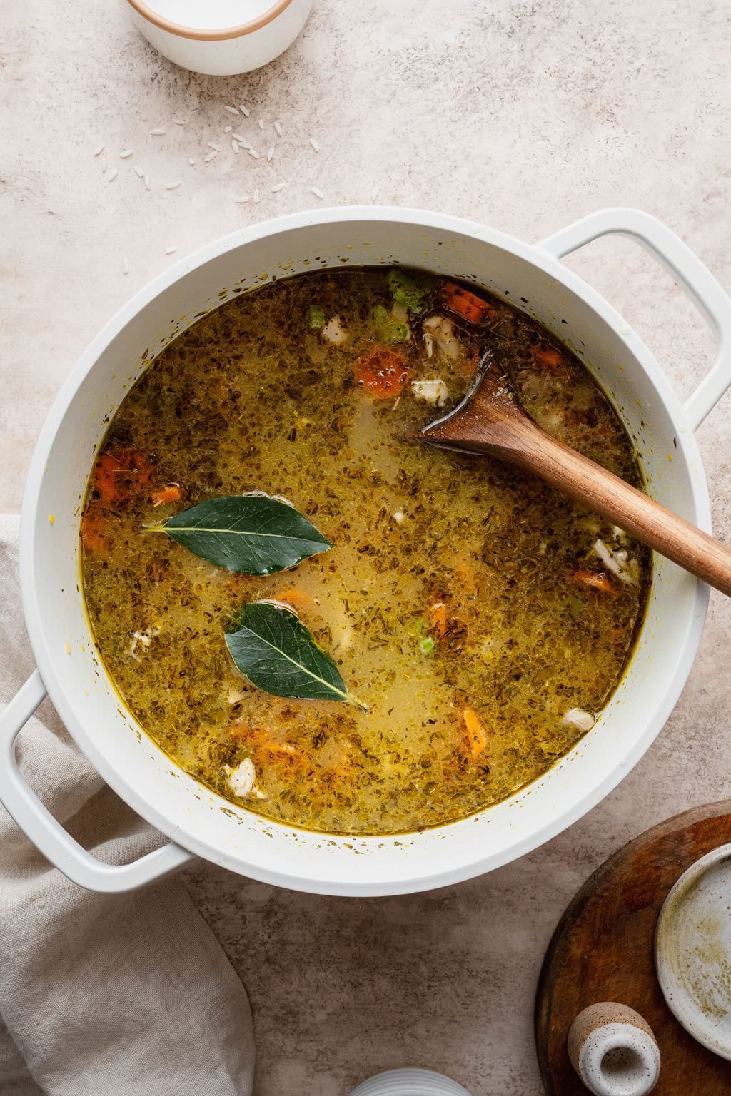 A pot of chicken and rice soup simmering with two bay leaves on top and a wooden spoon sticking out.
