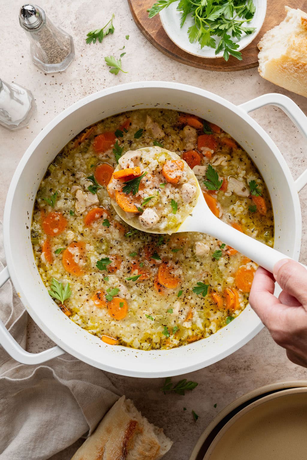 A hand lifting a spoonful of chicken and rice soup from a pot.
