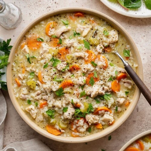 A bowl of chicken and rice soup with a spoon sticking out.
