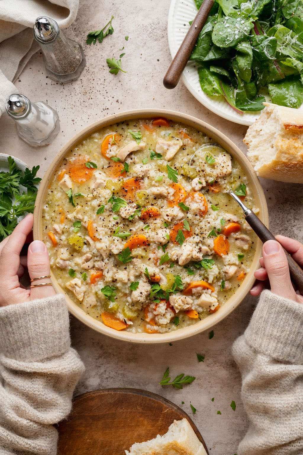 A woman's hands holding a bowl of chicken and rice soup, one hand dipping a spoon into the bowl.