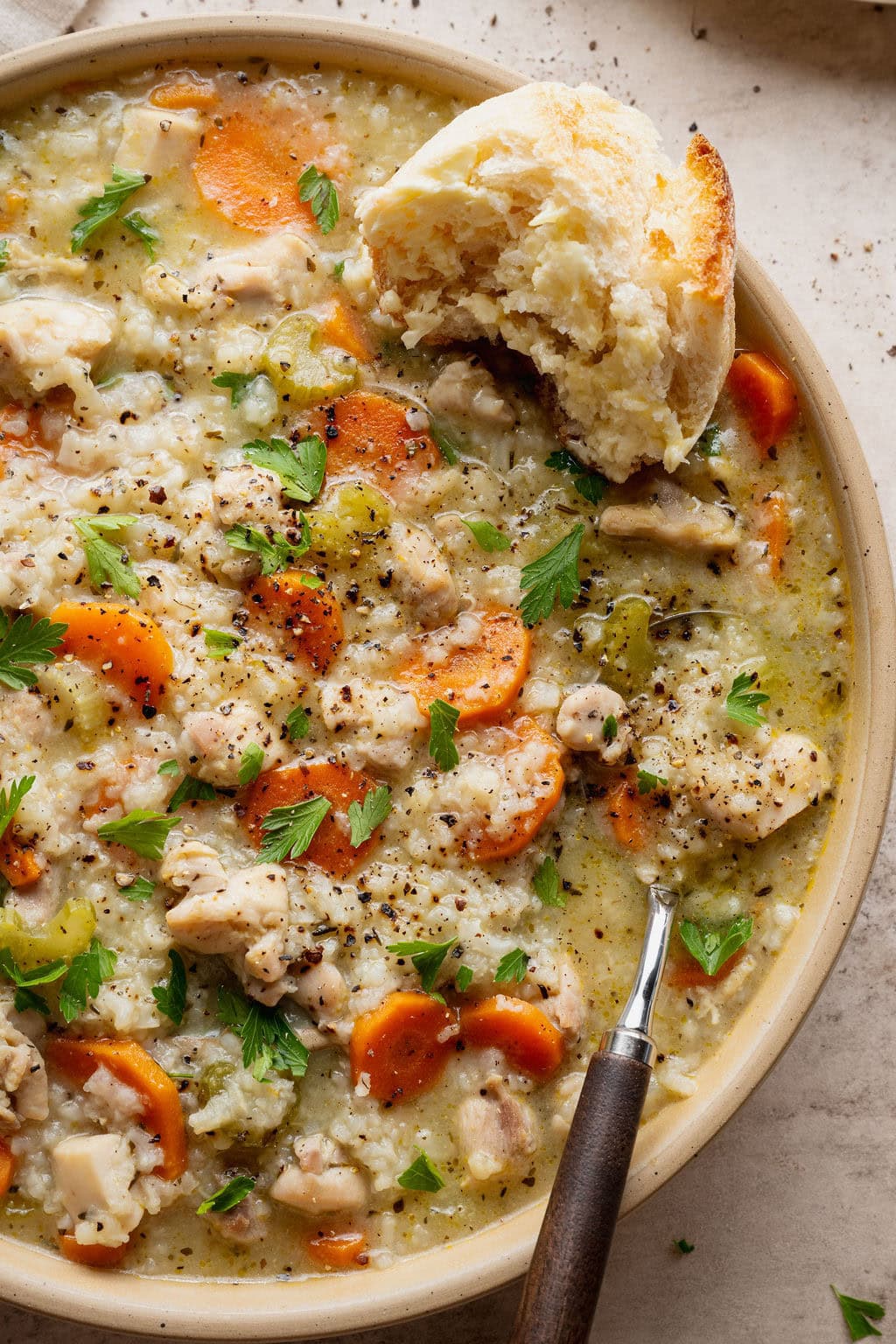 A bowl of chicken and rice soup topped with a partially eaten piece of crusty bread, a spoon sticking out.