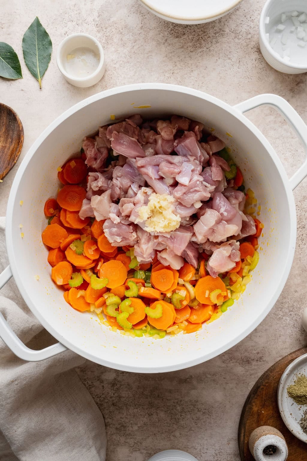 Raw chicken pieces and garlic being added to a pot of softened carrots, celery, and onions.